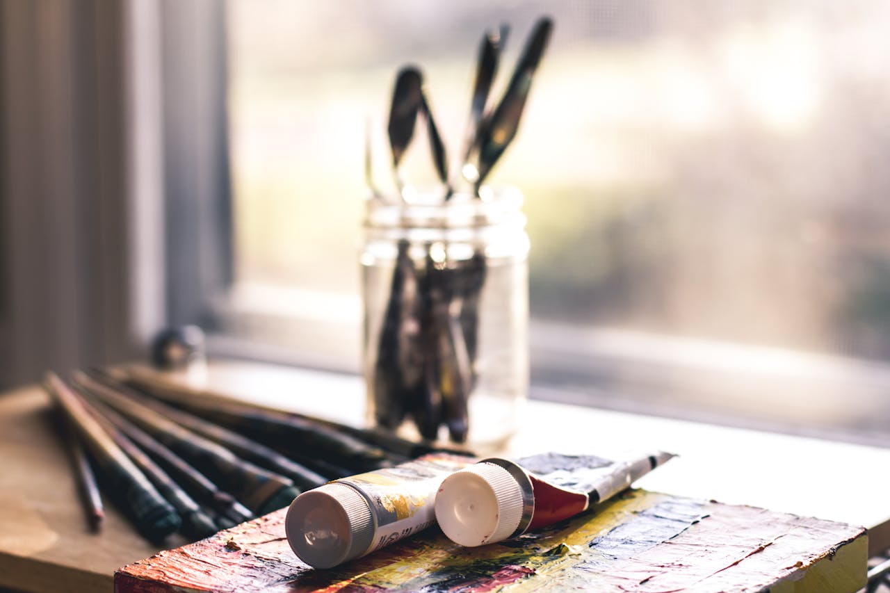 Sunlit table with art supplies, including brushes and paint tubes, ready for creative work.