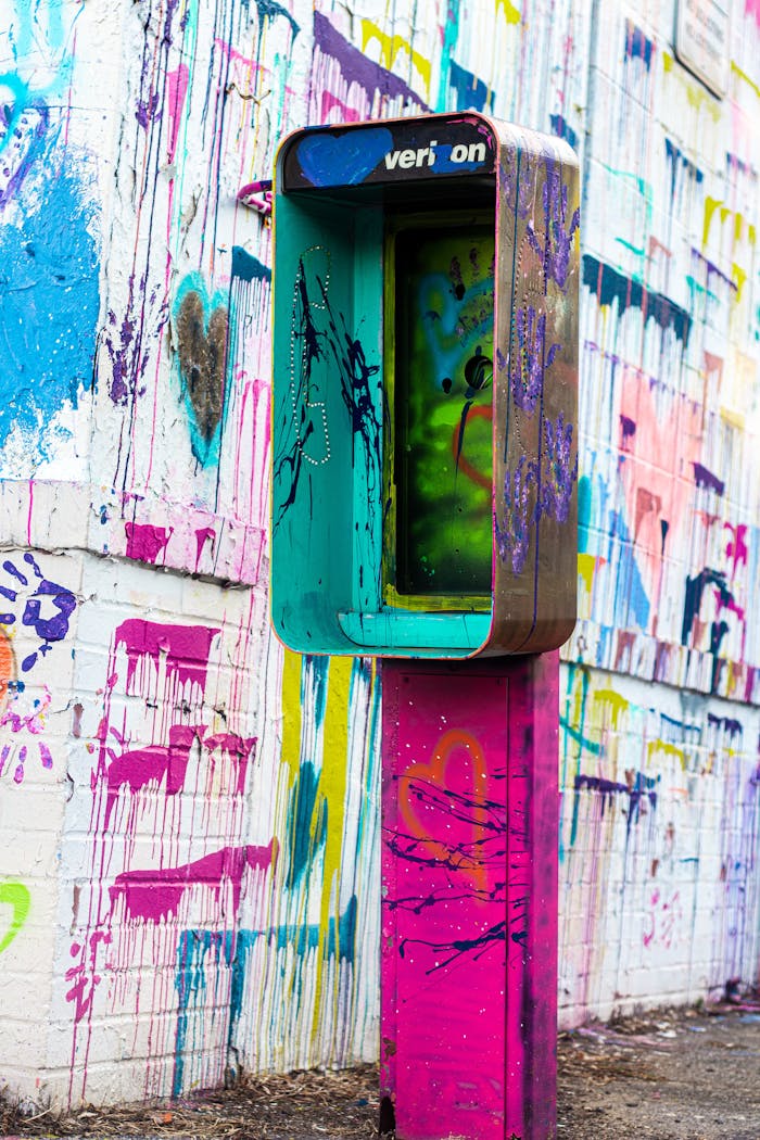 Vibrant graffiti covers a wall and vintage telephone booth in an urban setting.