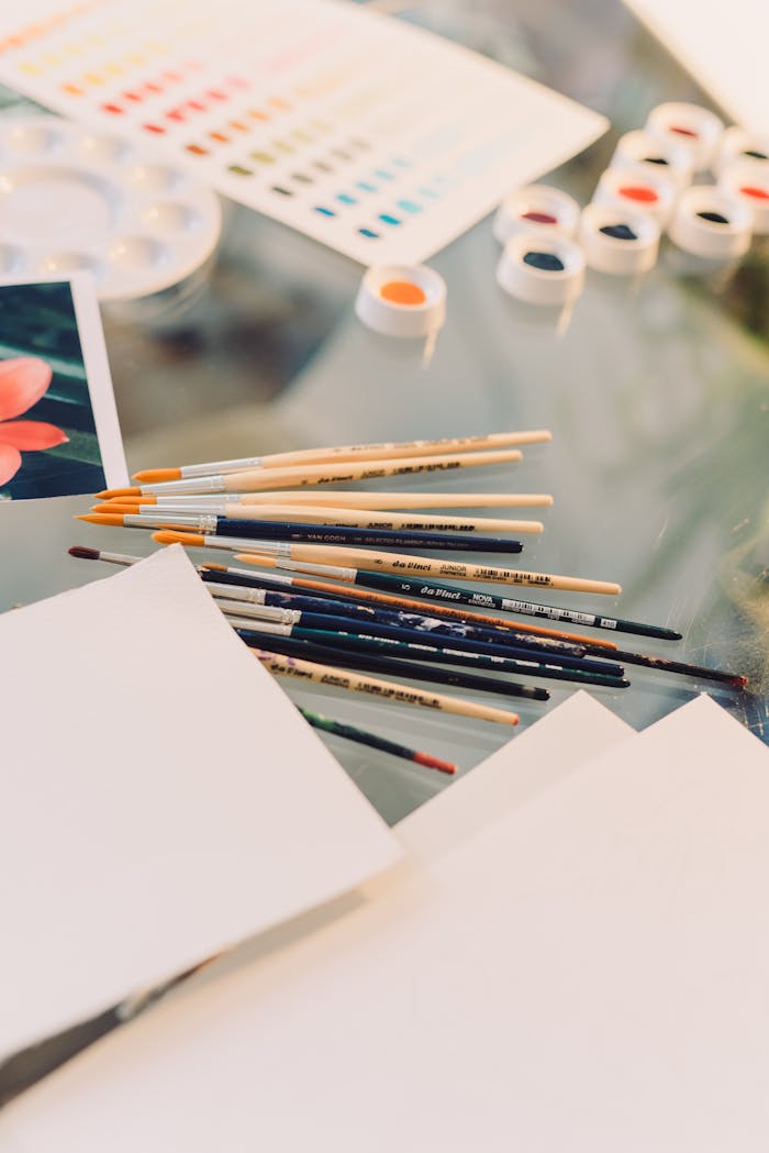 A collection of watercolor paints and brushes on a glass table for creative art projects.
