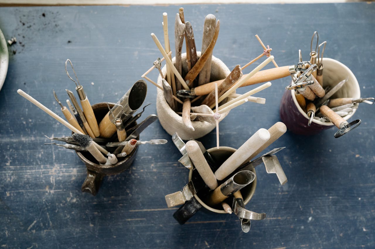 A top view of ceramic sculpting tools in mugs on a rustic wooden table, ideal for artists.